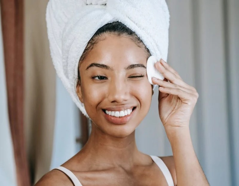 Smiling ethnic woman wiping face skin in morning