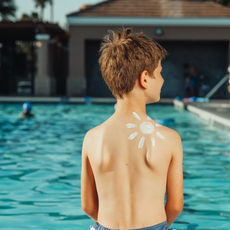 boy with sunscreen on shoulder sitting by the pool