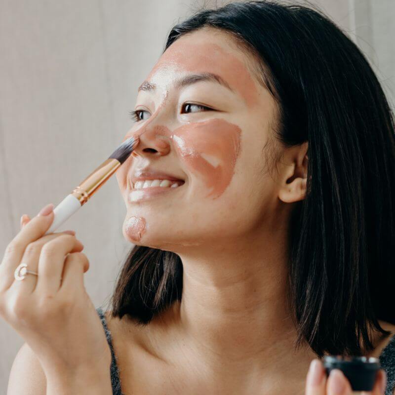 girl applying face mask with a brush 