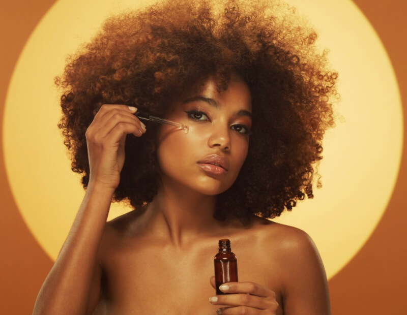 Young african woman applying serum to her face with dropper like a part of her skin care routine
